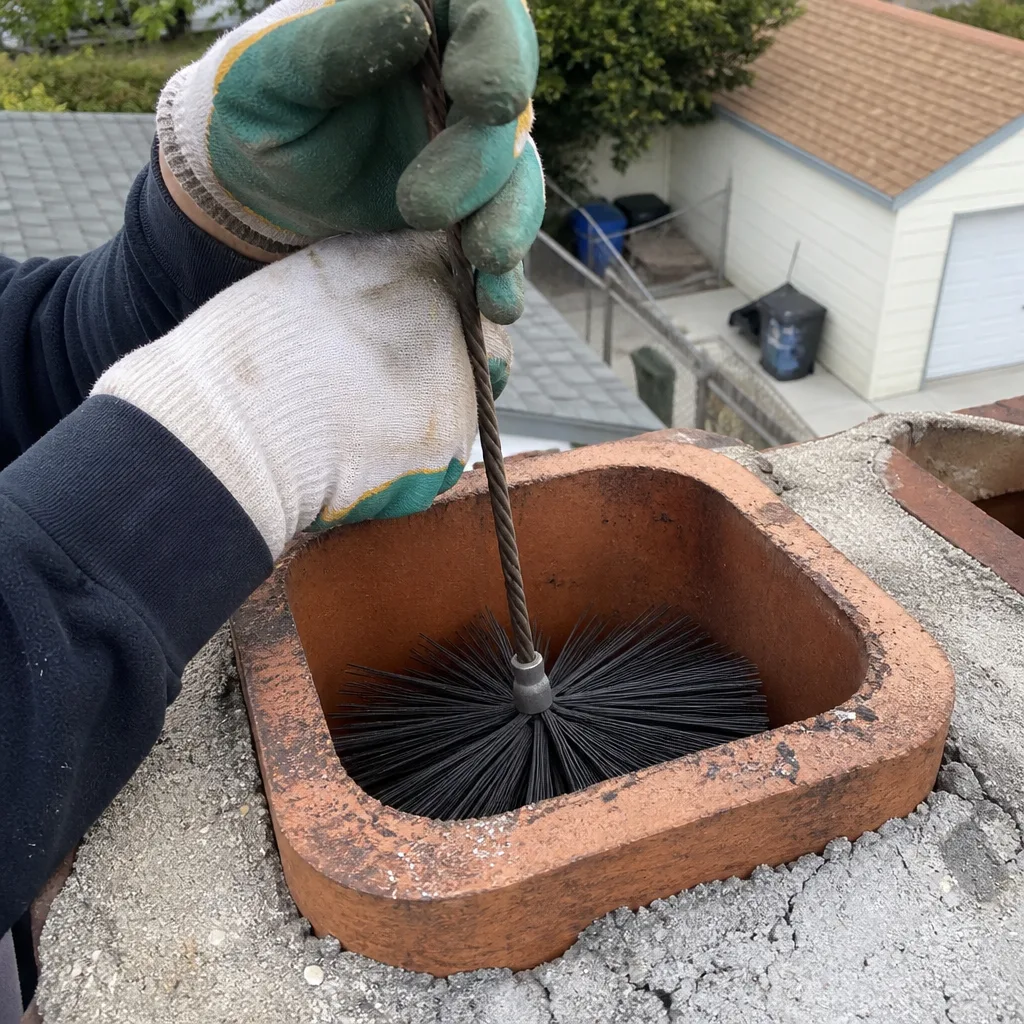 Professional chimney sweep cleaning a brick chimney flue with a wire brush